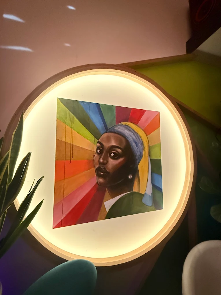 A wall-mounted painted portrait in a circular wooden frame, depicting a figure in a blue and gold head-wrap against a rainbow sunburst — one of the venue's conversation-piece artworks.